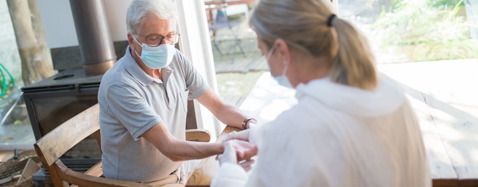 A home health nurse checking on an older woman seated in her own living room, the kind of visit Medicare covers at no cost for homebound patients in 2026