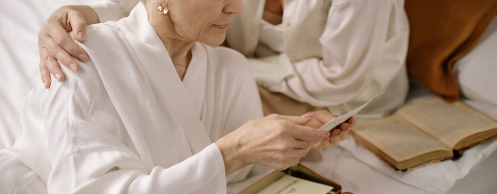 An older woman with gray hair and glasses reading a letter at a table covered with paperwork, the way a Mesa County resident might read a Medicare Advantage plan non-renewal notice in October